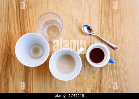 Des tasses à café sales, un cappuccino et un verre d'eau se tiennent sur une table en bois. Pause café. Pose à plat Banque D'Images