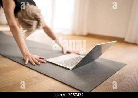 Femme 40+ pratique le yoga à la maison avec un ordinateur portable. Cours de yoga en ligne. Banque D'Images