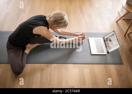 Femme 40+ pratique le yoga à la maison avec un ordinateur portable. Cours de yoga en ligne. Banque D'Images