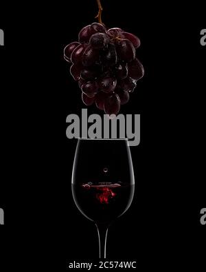 grappe de raisin mûr humide foncé et verres à vin isolés sur fond noir. des gouttes de jus tombent d'une grappe de raisins dans un verre de vin rouge Banque D'Images