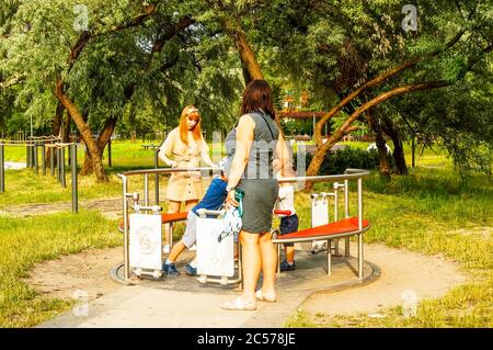 POZNAN, POLOGNE - 18 juin 2020 : les femmes et les enfants au rond-point d'un terrain de jeu dans le parc de Rataje par une journée ensoleillée Banque D'Images