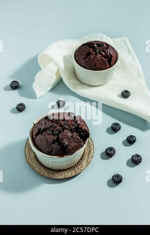 Muffins faits maison aux betteraves au chocolat avec baies dans des moules à gâteaux blancs sur fond bleu, serviette blanche, photo de lumière dure Banque D'Images