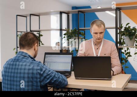 Deux CODEURS INFORMATIQUES travaillant sur l'ordinateur portable debout à la table au bureau Banque D'Images