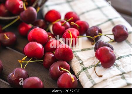 Foyer sélectif d'un gros plan d'un ensemble de cerises éparpillées sur une table en bois à côté d'un plat en toile. Concept de santé et de bonne alimentation Banque D'Images