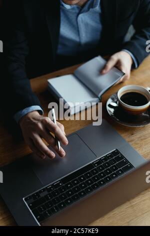 Homme d'affaires main sur un ordinateur portable pavé tactile tenant un stylo et un manuel pour des notes de recherche pour un projet Banque D'Images