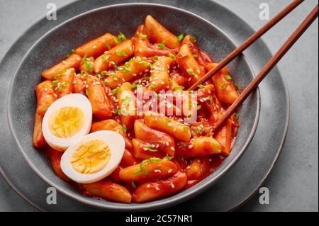 Tteokbokki avec œufs dans un bol gris sur une table en béton. Le tteok-bokki est un plat de cuisine coréenne composé de gâteaux de riz. Cuisine asiatique. Banque D'Images