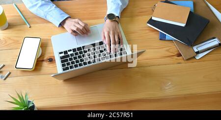 Au-dessus de la prise de vue, les mains d'une femme d'affaires tapissent sur un ordinateur portable au bureau en bois. Banque D'Images