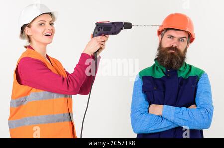 Femme avec le visage heureux exercices tête de l'homme, fond blanc. Homme avec un visage agacé dans un casque. Famille faisant la réparation, mari agacé par la femme. Le constructeur fait le trou dans la tête mâle. Concept de réparation ennuyeux. Banque D'Images