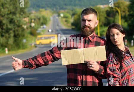 Couple avec les faces pensives Voyage par arrêt automatique. Couple amoureux voyageant en randonnée, espace copie. Homme et femme tentent d'arrêter la voiture avec un carton, pouces vers le haut. Concept aventure et randonnée. Banque D'Images