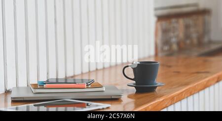 Une image rapprochée de la tasse à café est mise sur une planche en bois entourée d'un ordinateur portable, d'une tablette, d'un smartphone et d'un équipement. Banque D'Images