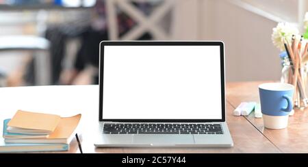 Ordinateur portable avec écran blanc vierge sur bureau en bois et entouré par une tasse de café, pile de livres, marqueurs, porte-crayon et po Banque D'Images