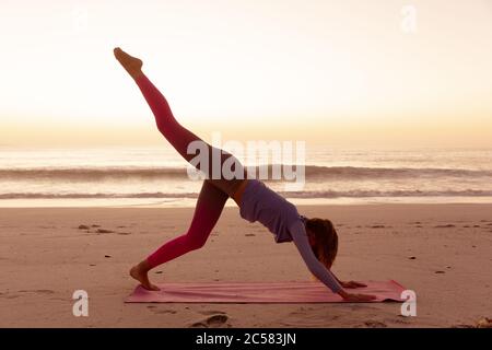 Femme pratiquant le yoga sur la plage au coucher du soleil Banque D'Images