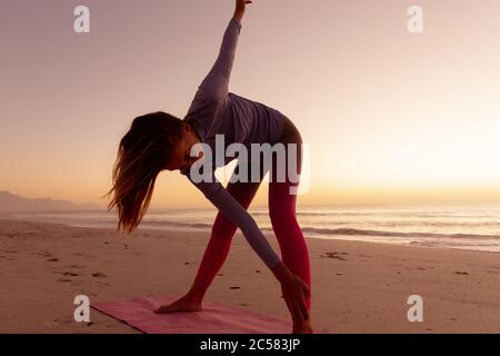 Femme pratiquant le yoga sur la plage au coucher du soleil Banque D'Images