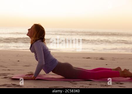 Femme pratiquant le yoga sur la plage au coucher du soleil Banque D'Images