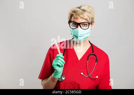 Portrait d'une femme médecin portant un masque facial montrant un thermomètre sur fond gris avec espace de copie zone publicitaire Banque D'Images