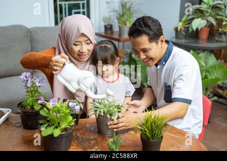 sa fille voit sa mère tenir un arrosoir tout en arrosoir des plantes et son père tenant une plante en pot sur la terrasse pour prendre soin des plantes Banque D'Images