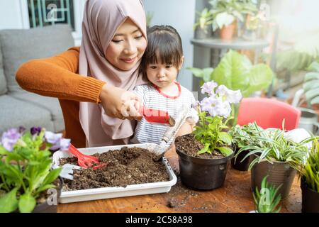 La mère asiatique aide sa fille à tenir une petite pelle remplie de terre pour cultiver des plantes en pot comme une activité à la maison Banque D'Images