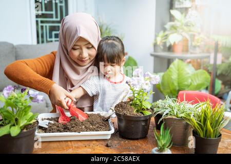 les mères asiatiques voilées aident leurs filles à tenir de petites pelles pour prendre le sol des plateaux pour cultiver des plantes en pots Banque D'Images