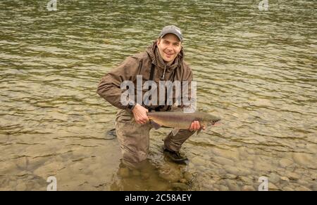 Pêcheur tenant un saumon sockeye au coucher du soleil sur une rivière en Colombie-Britannique, au Canada. Banque D'Images