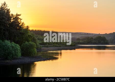 Magnifique coucher de soleil rural pittoresque sur des eaux calmes (arbres boisés et reflets du ciel orange coloré) - Fewston Reservoir, North Yorkshire, GB. Banque D'Images