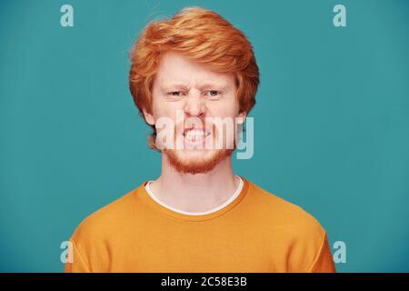 Portrait d'un homme à tête rouge en colère avec une barbe frognée face en agression contre fond bleu Banque D'Images