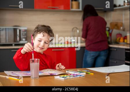 Happy boy dessine la peinture sur la cuisine tandis que sa mère cuisine Banque D'Images