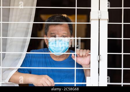 Homme chinois anxieux avec masque facial auto-isolation quarantaine à la maison pendant 14 jours par crainte du virus Covid-19 de contact Banque D'Images