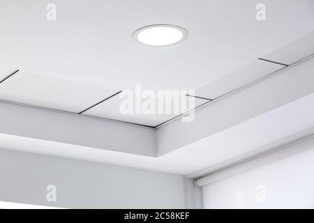 plafond à plusieurs niveaux avec protubérances tridimensionnelles et plafond en carrelage suspendu avec lumière led ronde intégrée dans le coin de la pièce, à proximité Banque D'Images