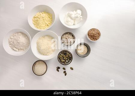 Ingrédients de cuisson pour un pain sain à faible teneur en glucides avec du fromage blanc, du son d'avoine, de la farine d'amande et de diverses graines sur une table blanche, vue en grand angle de l'ab Banque D'Images