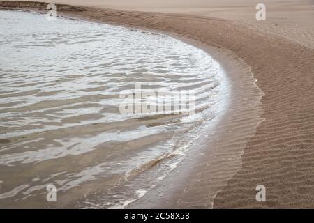 De petites vagues aux reflets flamboyants se sont enferchies contre le balayage des courbes d'une plage de sable, St Andrews, Écosse Banque D'Images