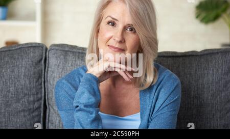 Portrait de la belle femme blonde de 50 ans est assise sur un canapé à la maison Banque D'Images