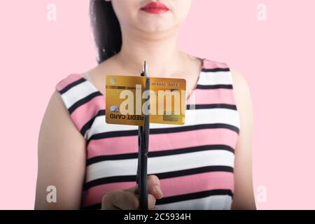 Portrait d'une jeune femme asiatique coupant une carte de crédit avec des ciseaux pour arrêter de dépenser sur le fond rose Banque D'Images