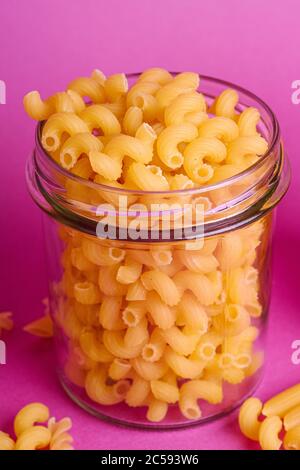 Un pot en verre avec des pâtes cavataappi au blé doré sur fond rose minimal, vue en angle macro Banque D'Images