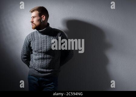 Portrait studio d'un jeune homme barbu de vingt-cinq ans. Dans un pull chaud d'hiver, fièrement, gris, regarde loin. Sur un fond noir. Dans un Banque D'Images