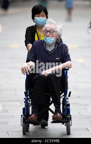 Une femme portant un masque chirurgical bleu pousse un homme âgé dans un fauteuil roulant portant un masque chirurgical bleu pendant le verrouillage du coronavirus Banque D'Images