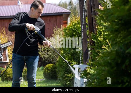 40s homme lave des balançoires en bois dans le jardin de maison de campagne avec un nettoyeur haute pression Banque D'Images