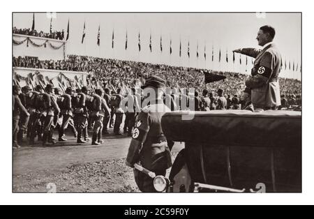 Adolf Hitler portant un brassard de croix gammée lors d’un rassemblement du Parti nazi de Nuremberg des années 1930, debout derrière son monoplace Mercedes, qui saluait les troupes de l’aile militaire du parti politique NSDAP Banque D'Images