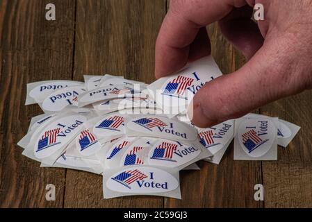 Denver, CO--30 juin 2020; main de l'électeur atteignant dans une pile de rouge blanc et bleu ovale j'ai voté des autocollants pour placer un sur la chemise après avoir fait le bulletin de vote et Banque D'Images