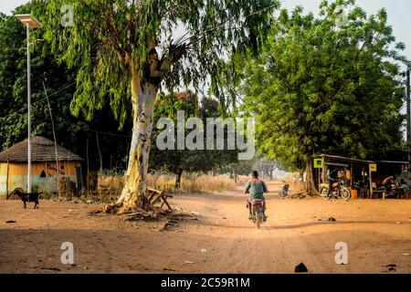 Afrique, Afrique de l'Ouest, Bénin, Natitinqou. Un homme en moto traverse un village africain Banque D'Images
