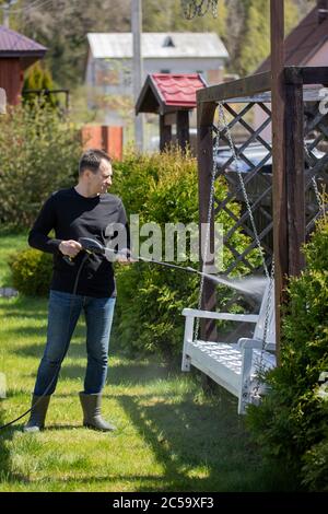 40s homme lave des balançoires en bois dans le jardin de maison de campagne avec un nettoyeur haute pression Banque D'Images