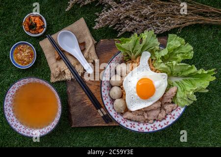 Faire bouillir les nouilles aux œufs avec de la boule de porc, du porc haché, des œufs frits, des légumes et des soupes dans un bol et un bâtonnet à base de cuillère et de bois. Soupe de nouilles thaï Banque D'Images