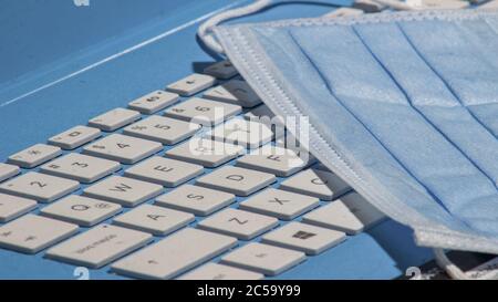 Gros plan d'un masque médical posé sur le clavier blanc d'un virus pc portable bleu sur le lieu de travail Banque D'Images