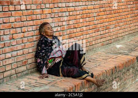 Une femme népalaise âgée repose sur un petit mur de briques à la place Durbar à Bhaktapur, au Népal Banque D'Images