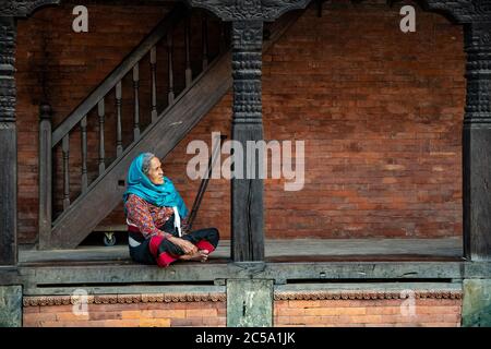 Femme népalaise âgée assise sur la véranda de sa maison typique de style Nepa à Bhaktapur, au Népal Banque D'Images