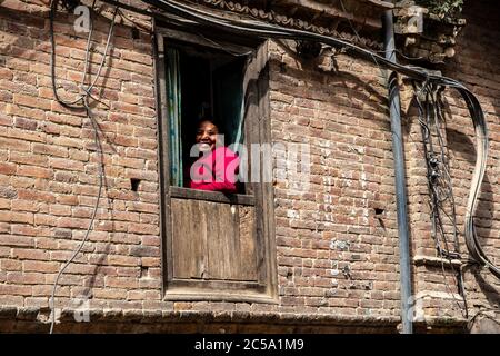 La femme de Nepa sourit en regardant par la fenêtre de sa maison en briques typique dans le centre du village de Thimi, la vallée de Katmandou, au Népal Banque D'Images