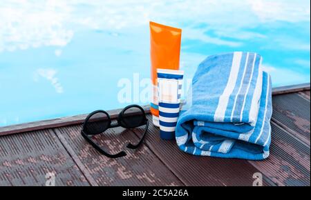 lunettes de soleil, tube de crème solaire, serviette bleue près de la piscine, fond tropical Banque D'Images