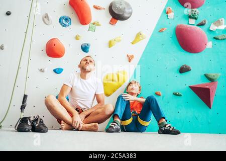 Père et fils adolescent assis près du mur d'escalade intérieur. Ils se reposent après l'escalade active. Image de concept de parentalité heureuse. Banque D'Images