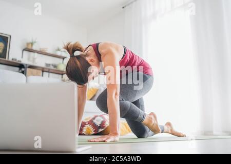 Posez la femme causasienne sportive en bonne santé sur un tapis dans une pose de yoga, faisant des exercices de respiration, regardant les cours de yoga en ligne sur ordinateur portable. Des gens en bonne santé et Banque D'Images