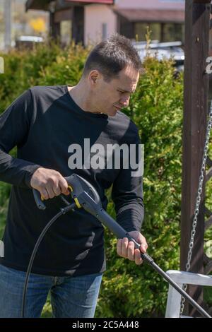 40s homme lave des balançoires en bois dans le jardin de maison de campagne avec un nettoyeur haute pression Banque D'Images