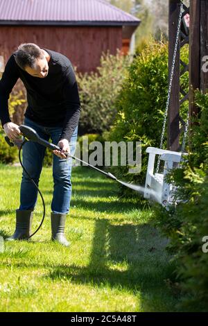 40s homme nettoie les balançoires dans le jardin de maison de campagne avec un nettoyeur haute pression Banque D'Images